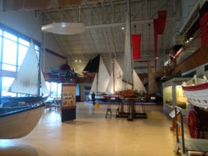 A big open room with boats on the floor, and suspended from the ceiling.