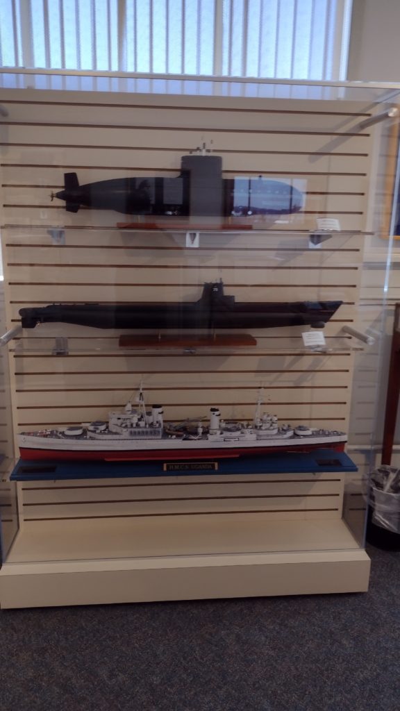 A glass case containing large models of two different submarines and a World War II cruiser.