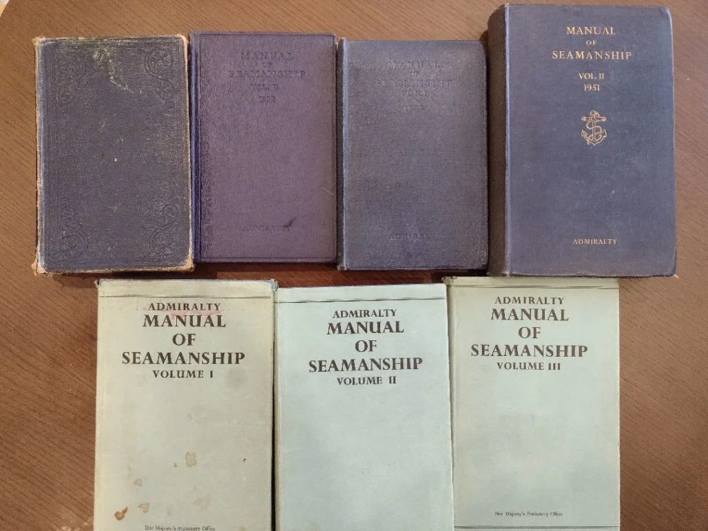 7 books lie on a table, they have blue covers that say "Manual of Seamanship" and "Admiralty". They date from 1913 to the 1960s