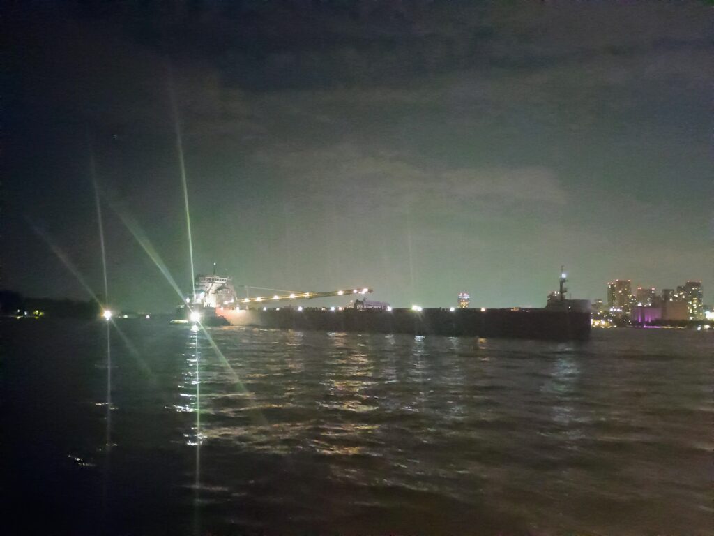 Freighter with the bright lights of the tug beside it