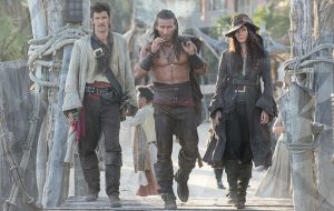 three pirates (two men and a woman) walking along a pier towards the camera