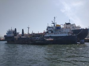 A tug is tied up to a small tanker and a larger ship. All three are derelict.