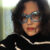 A woman with dark hair, blue sparkly glasses and a striped sweater
